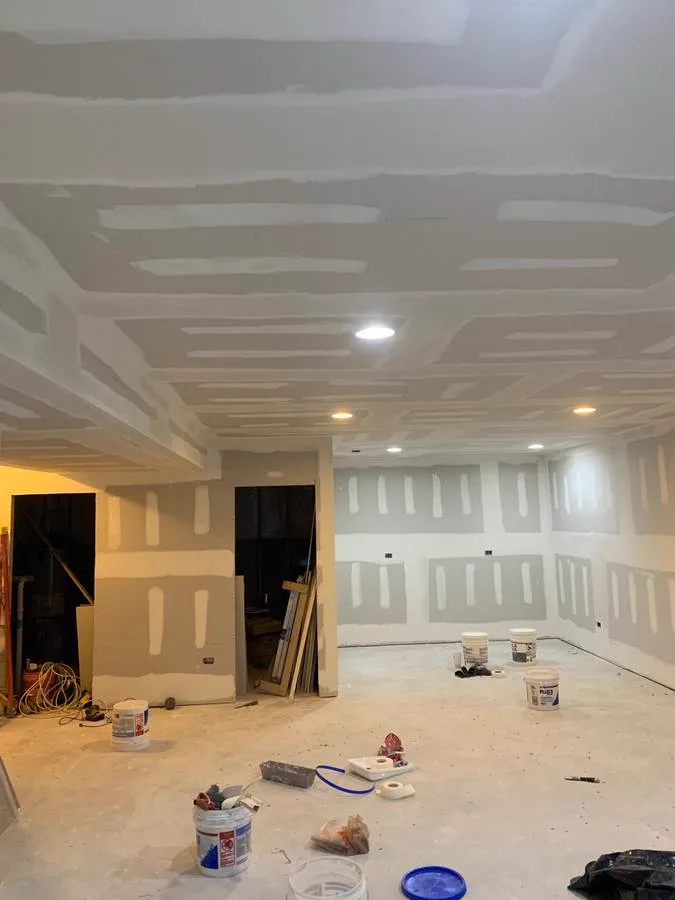 Freshly hung drywall on walls and ceiling of an unfinished room, joint-compound buckets on the floor